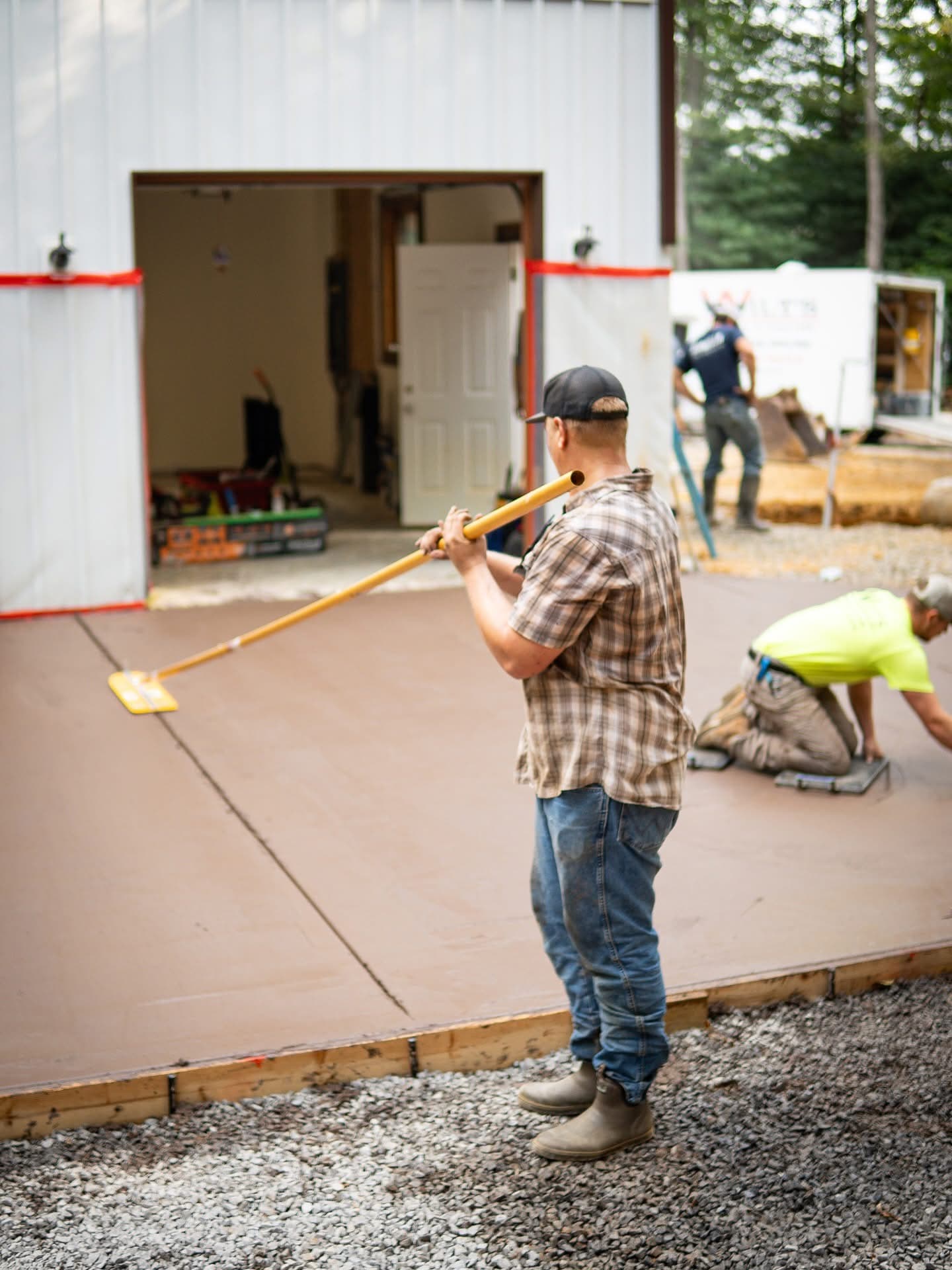 Construction worker smoothing a freshly poured concrete slab with a long-handled bull float tool.